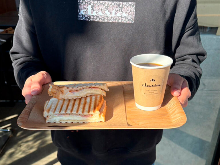 スタッフが手に持ったホットサンドとホットコーヒーのセット。