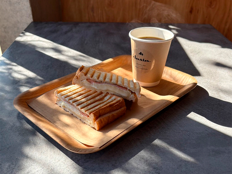 店内のテーブルに並ぶホットサンドとホットコーヒーのセット。モールテックスのテーブルとやわらかい自然光