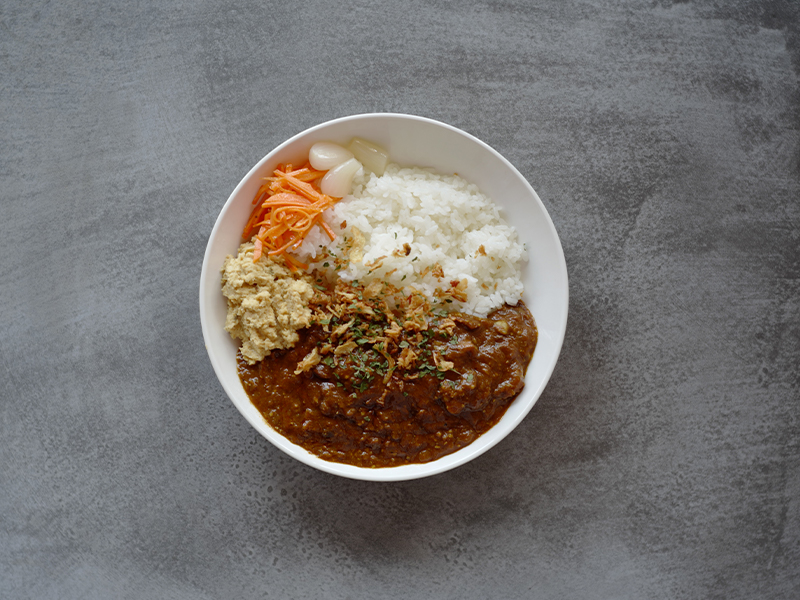 白いお皿に盛りつけられた「パイカカレー」。濃い茶色のルーの中には、じっくり煮込まれてとろけるように柔らかくなった豚バラ軟骨（パイカ）がゴロゴロと入っており、白ごはんと一緒に提供されている。付け合わせには彩りのよい野菜も添えられ、食欲をそそる盛りつけ