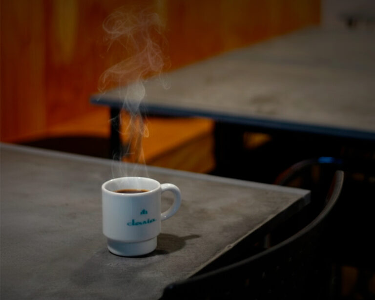 湯気の立つコーヒーカップがモールテックスのテーブルに置かれた落ち着いたカフェの一角。