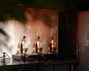 カフェのカウンターに並ぶサイフォン器具。温かな光に照らされ、ガラスフラスコが静かに抽出を行っている様子