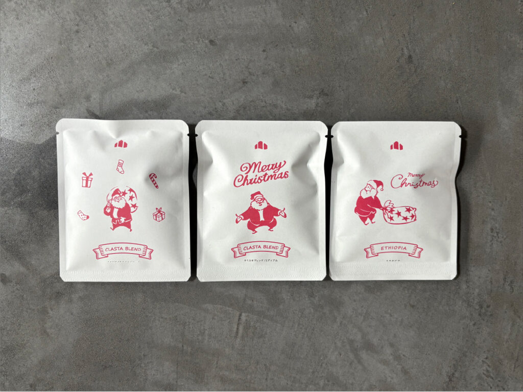 コンクリート調のテーブルの上に、クリスマス限定デザインのドリップパックが縦に3種類並んでいる。エチオピア、クラスタブレンド（ミディアム）、クラスタブレンド（ディープ）の3種類